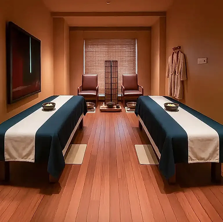 Elegant couple massage room at Tattva Wellness Spa, SLN Terminus Hyderabad, featuring twin massage beds with navy and beige linens, wooden flooring, and a serene ambience.
