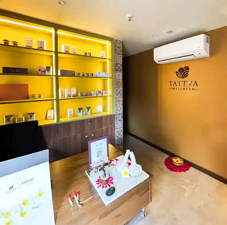 Reception area of Tattva Wellness Spa, Fairfield by Marriott Calangute Goa, showcasing a wooden desk, bright yellow product display shelves, and elegant decor reflecting a warm Goan hospitality ambiance.