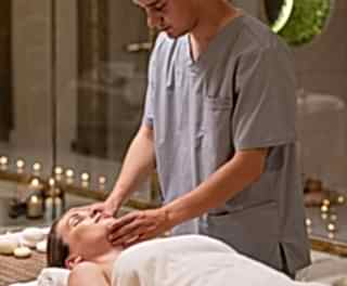 Healer at Tattva Spa in Bangalore performing a relaxing facial massage in a serene, candle-lit spa setting.